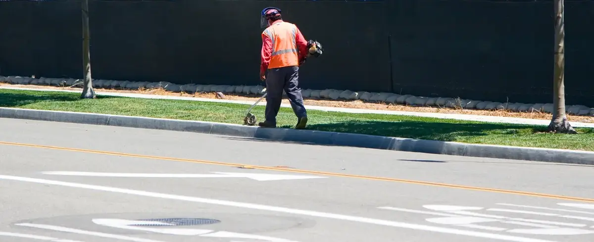 Crew member edging grass along a curb